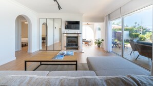 Un salon moderne doté d’une cheminée, d’un téléviseur et d’une grande porte vitrée donnant sur une terrasse extérieure.