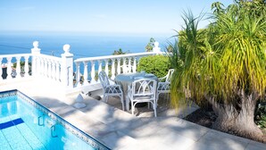Un espace aménagé au bord de la piscine, avec une clôture blanche, une table et des chaises, et une vue sur la mer.