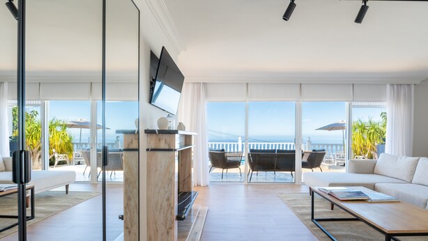 Un salon moderne doté d’une grande fenêtre, d’un téléviseur à écran plat et offrant une vue sur la mer.