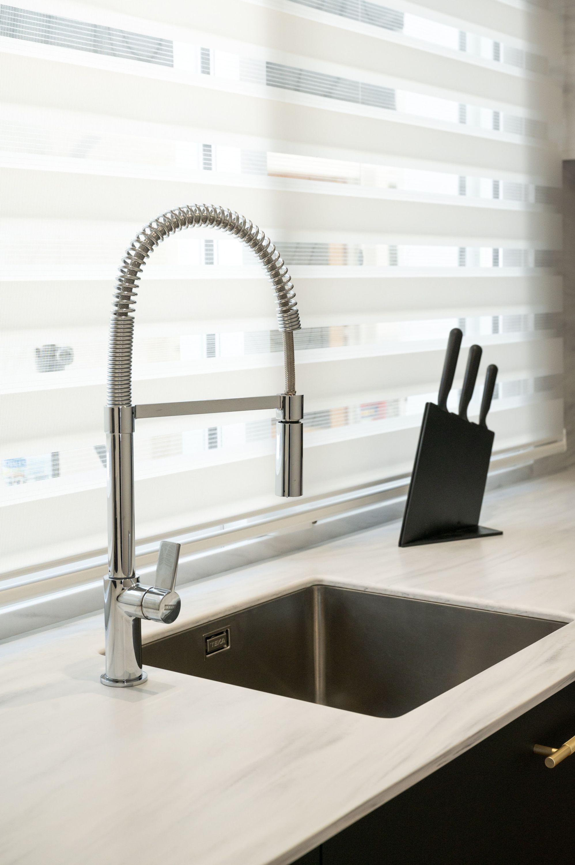Una cocina moderna con un lavamanos de acero inoxidable, un grifo curvo y un bloque de cuchillos negro.