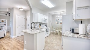 A modern kitchen with white cabinetry, a central island, and a dining area with white chairs.