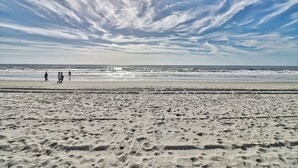 A beach with footprints in the sand and a few people walking.