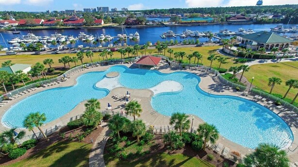A large, irregularly shaped swimming pool surrounded by palm trees and a marina with boats.