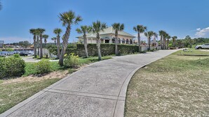 A curved concrete pathway leading to a building with a light-colored facade and arched windows, surrounded by palm trees and greenery.