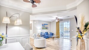 A spacious living room with a blue sofa, a white armchair, a dining table, and a ceiling fan.