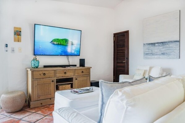 A living room with a flat-screen TV, wooden cabinet, white sofa, and a painting on the wall. - Cozy Beach Villa at Rio Mar (Rio Grande)