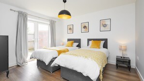 A modern bedroom with two beds, a large window, and a ceiling light.