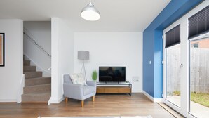 A modern living room with a staircase, a flat-screen TV, and a large window with a view of the outside.