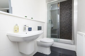 Ein modernes Badezimmer mit Waschbecken, Toilette und Dusche, alles in Weiß.
