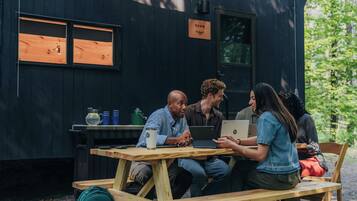 Een groep mensen zit aan een houten picknicktafel met laptops, voor een zwart gebouw met een bord waarop 'DAWN' staat.