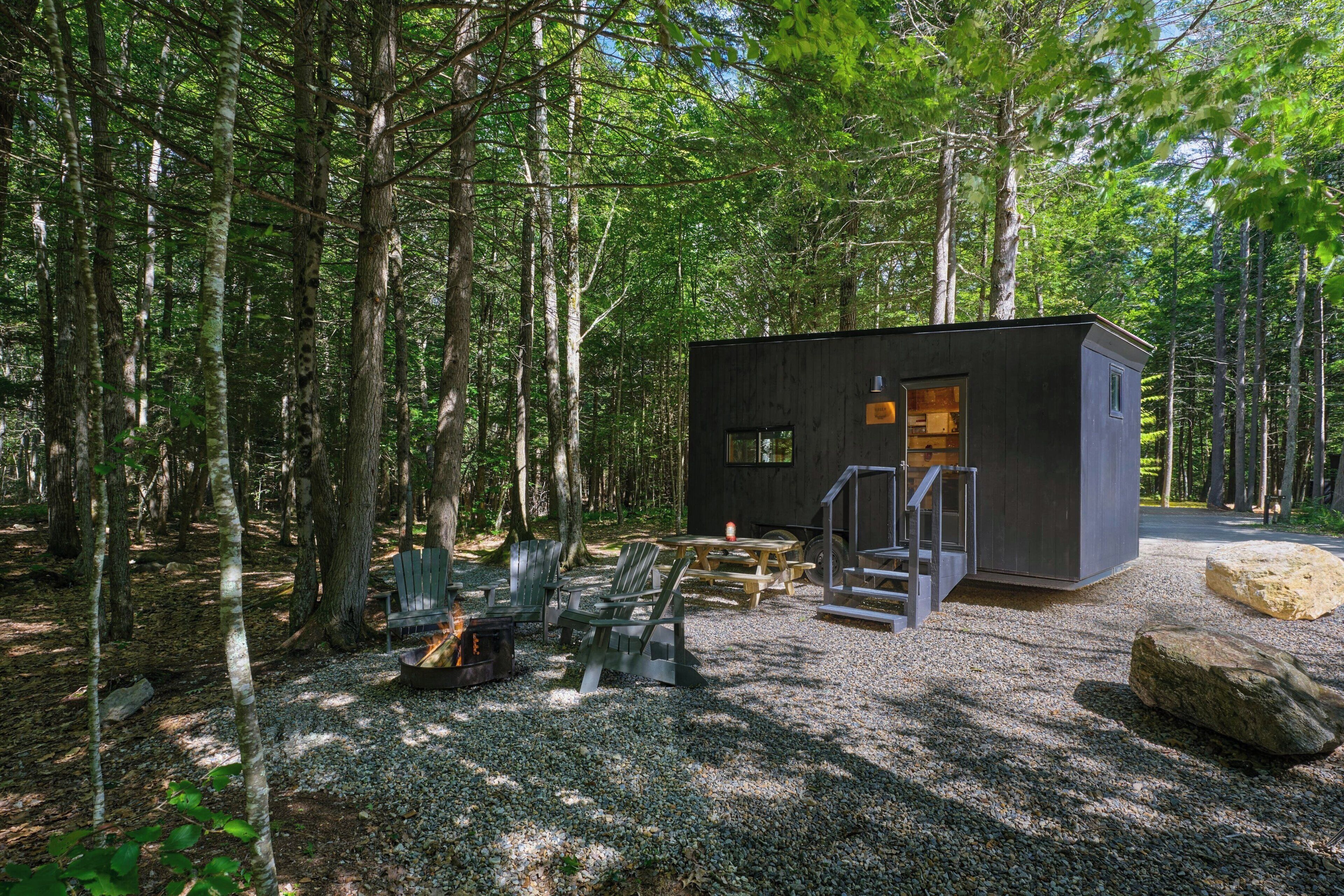 A cabin with a gravel ground, wooden deck, and a fire pit.