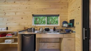 A compact kitchen with wooden walls, a window with a view of greenery, a sink, a stove, and a dishwasher.
