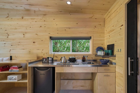 Une cuisine compacte aux murs en bois, une fenêtre donnant sur un paysage verdoyant, un évier, une cuisinière et un lave-vaisselle.