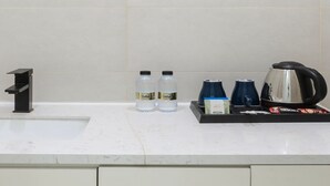 Un lavamanos con grifo negro, dos botellas de agua, una cafetera y una caja de café Nescafe.