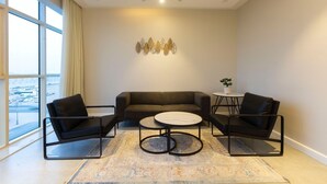 Una sala de estar moderna con un sofá, dos sillones, una mesa de centro y vistas a un paisaje urbano a través de amplios ventanales.