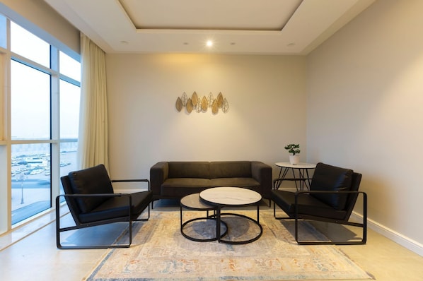 Una sala de estar moderna con un sofá, dos sillones, una mesa de centro y vistas a un paisaje urbano a través de amplios ventanales.