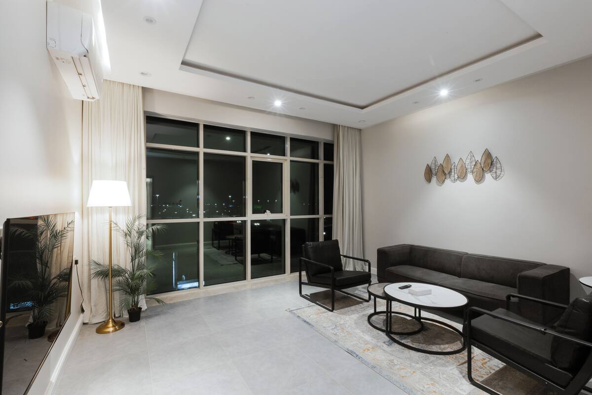 A modern living room with a large window, a sofa, a coffee table, and a floor lamp.