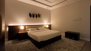 Una habitación de hotel con una cama grande, dos mesitas de noche con lámparas, una lámpara de pared y suelo alfombrado.