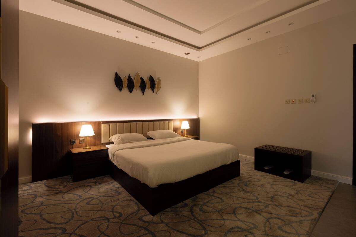 A hotel room with a large bed, two bedside tables with lamps, a wall-mounted light fixture, and a carpeted floor.