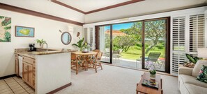 A spacious living area with a kitchen, dining table, and a sliding glass door leading to a garden.