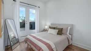 Una camera da letto con un letto, un comodino, una lampada, una finestra con tende e vista all'esterno.