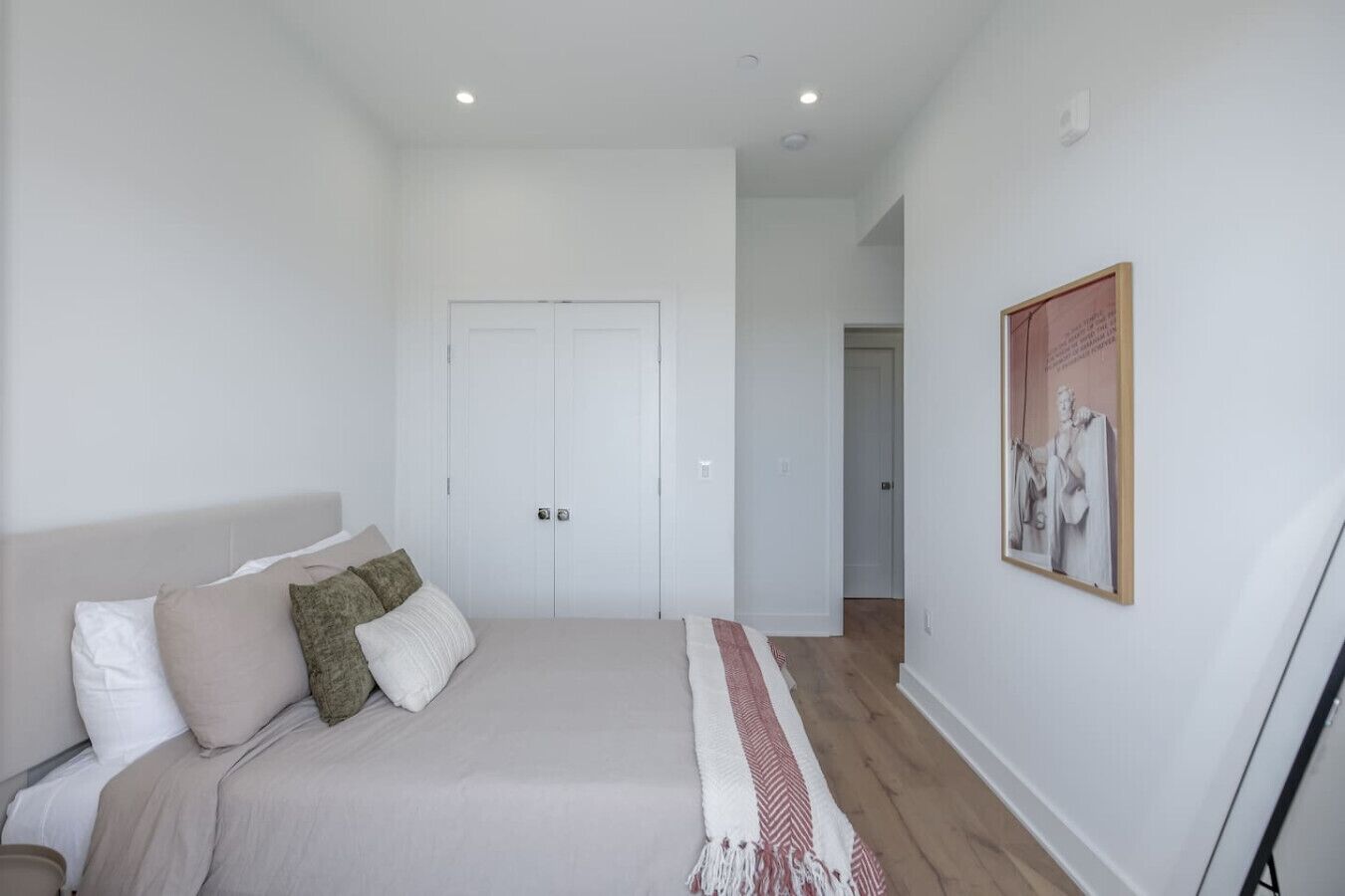 Quarto com cama, almofadas, guarda-roupa, porta e um quadro na parede.