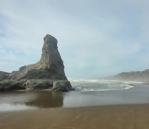 A coastal landscape with a prominent rock formation and waves crashing onto the shore.