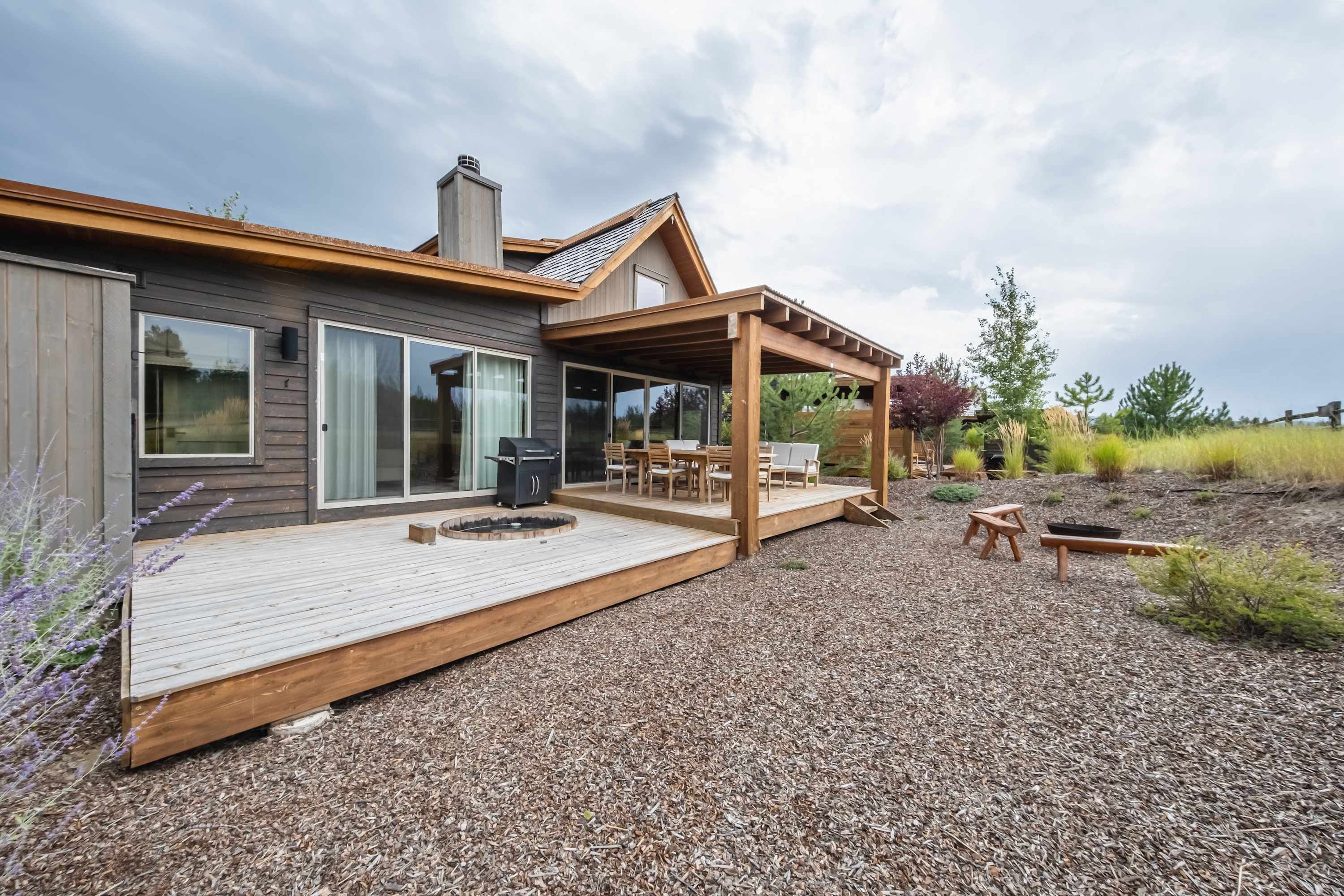 A modern house with a wooden deck, large windows, and a covered outdoor seating area.