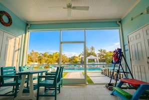 A covered patio with a view of a swimming pool, outdoor seating, and a children's play area.