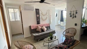 Una sala de estar con un sofá gris, dos sillas de mimbre, una mesa de centro y un ventilador de techo.