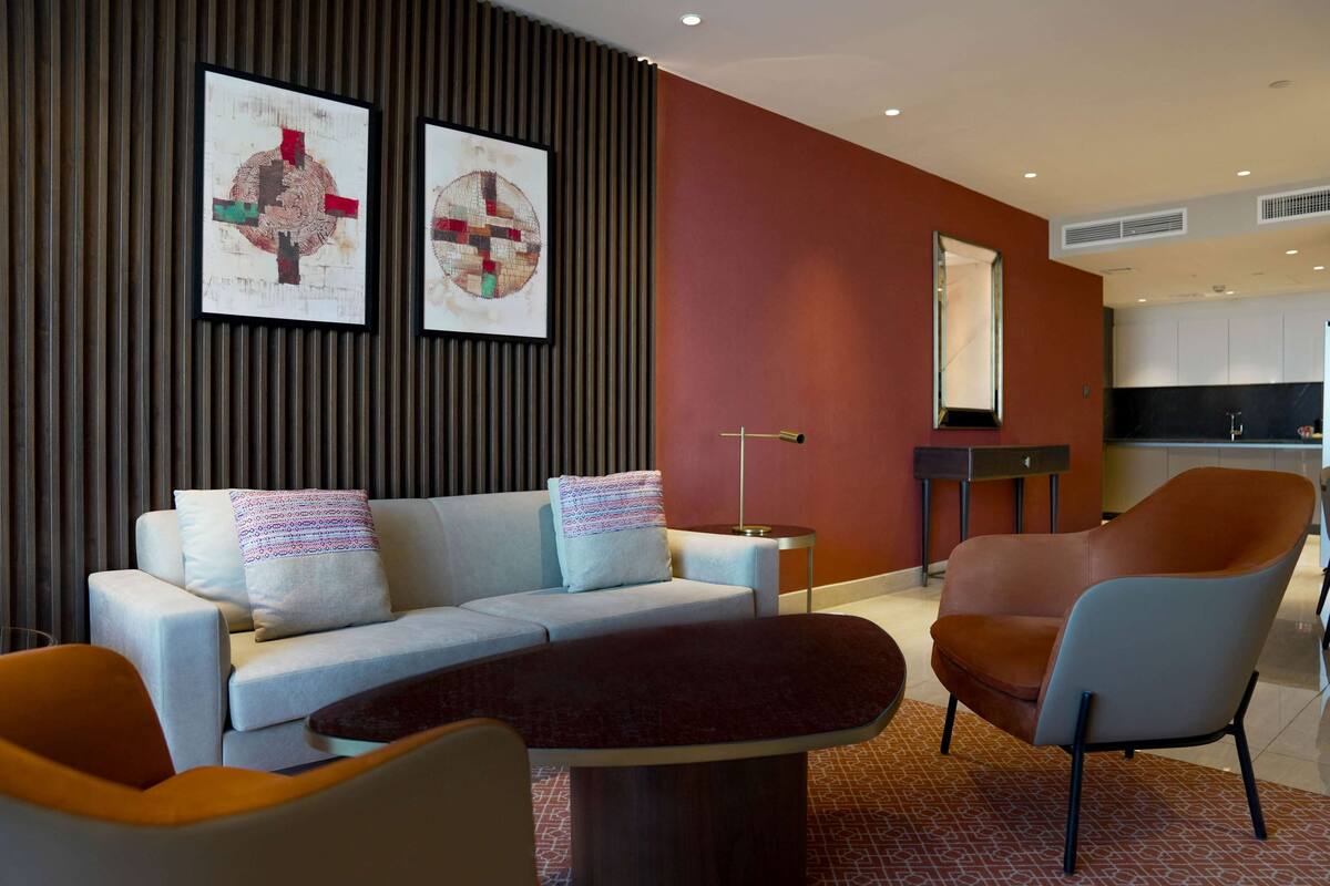 A modern living room with a sofa, armchairs, a coffee table, and two abstract paintings on the wall.