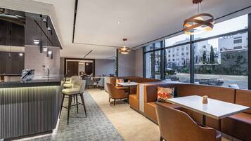 A modern restaurant with a bar area, seating with cushioned booths, and large windows offering a city view.