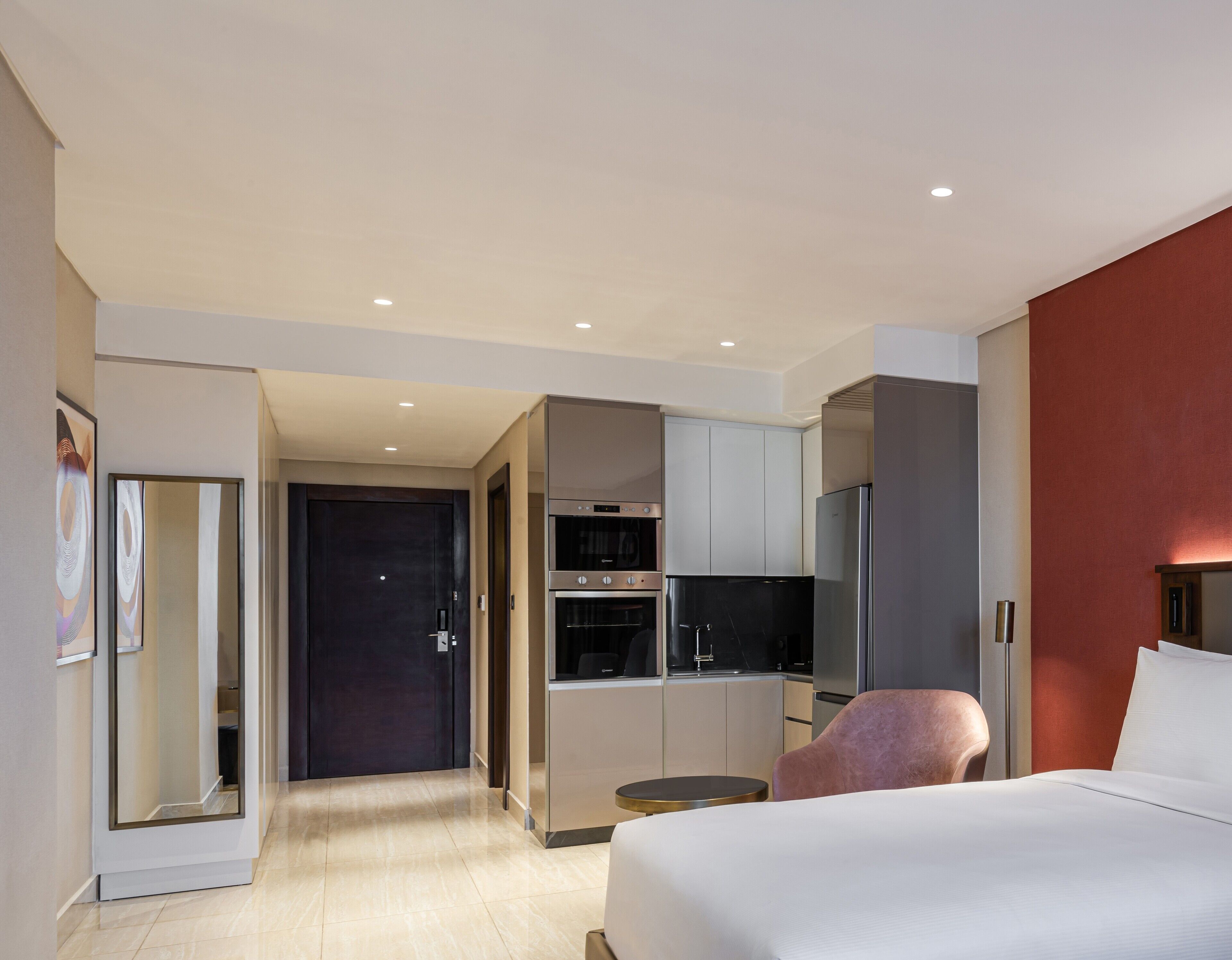 Une chambre d’hôtel moderne dotée d’un grand lit, d’une petite table ronde, d’une télévision, d’un minibar et d’un coin cuisine séparé.