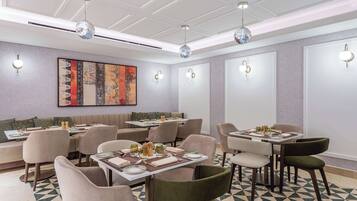 A modern dining area with tables set for meals, ambient lighting, and a large abstract painting on the wall.