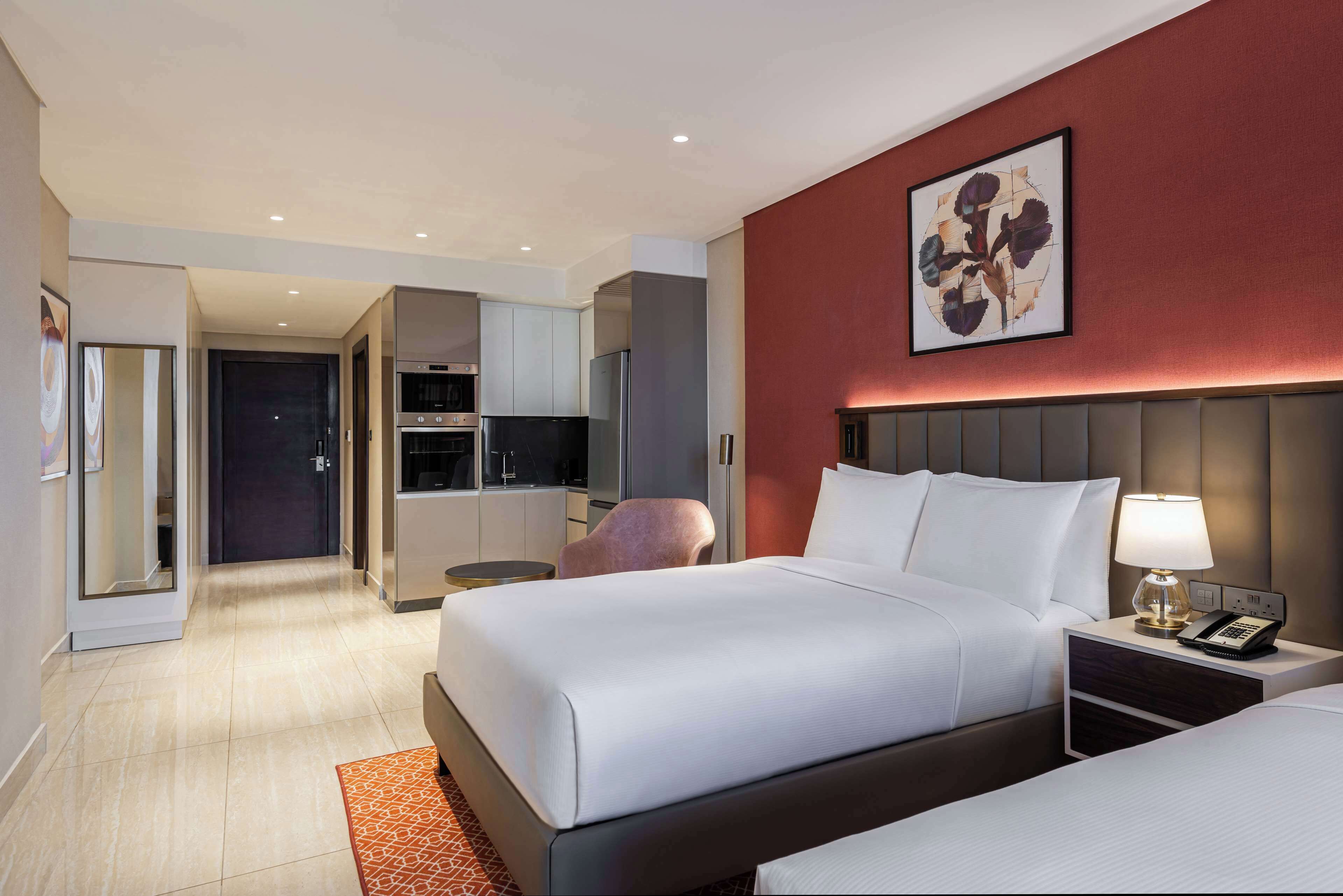 A hotel room with a bed, bedside table, lamp, and a painting on the wall.