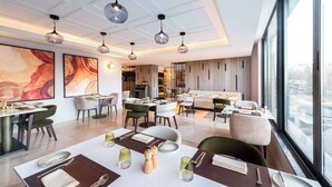 A modern dining area with tables set for service, pendant lighting, and large windows offering a city view. - Doubletree By Hilton Amman Hotel & Residences (Amman)