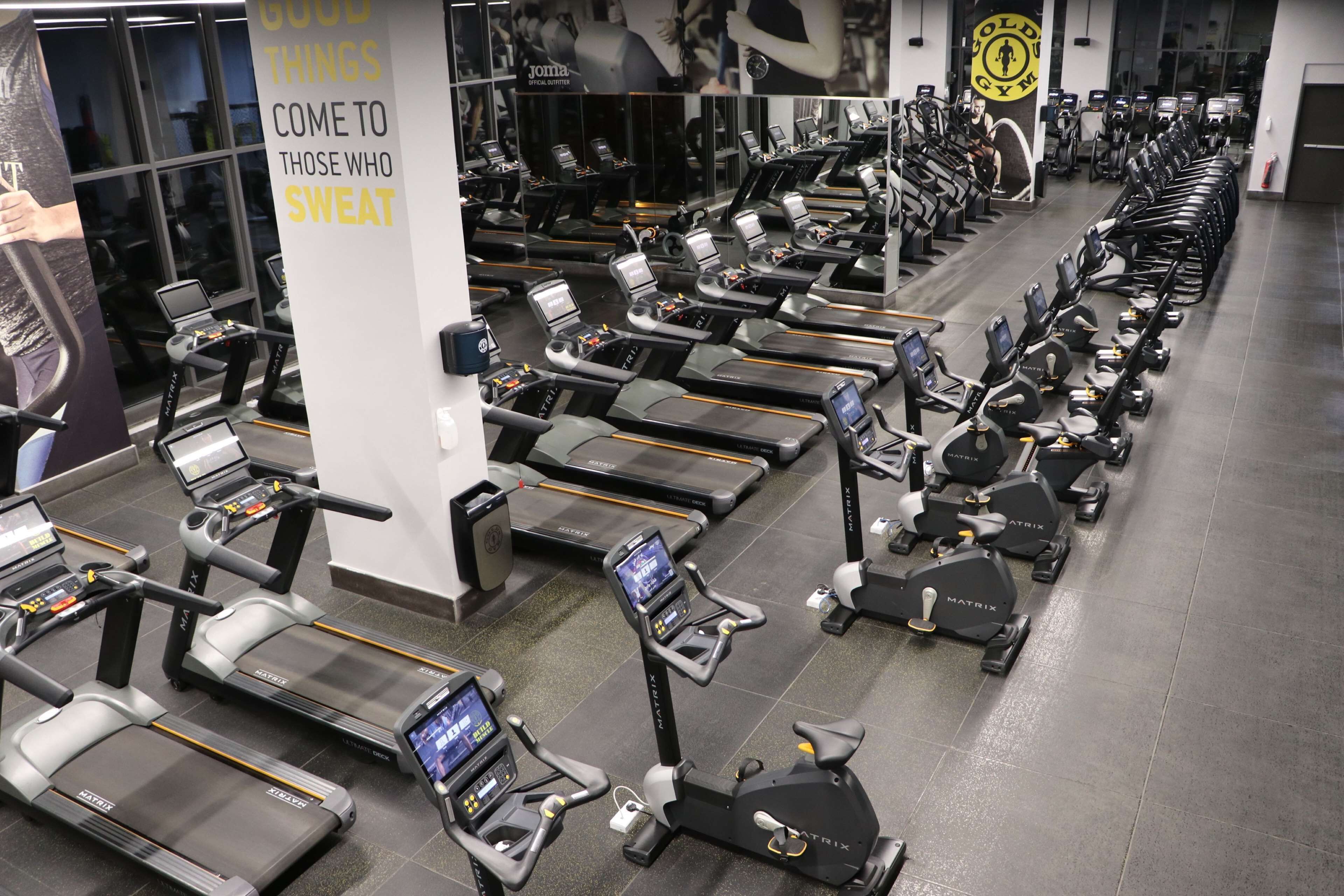 Et fitnessrum med flere løbebånd og crosstrainere stillet op i rækker.
