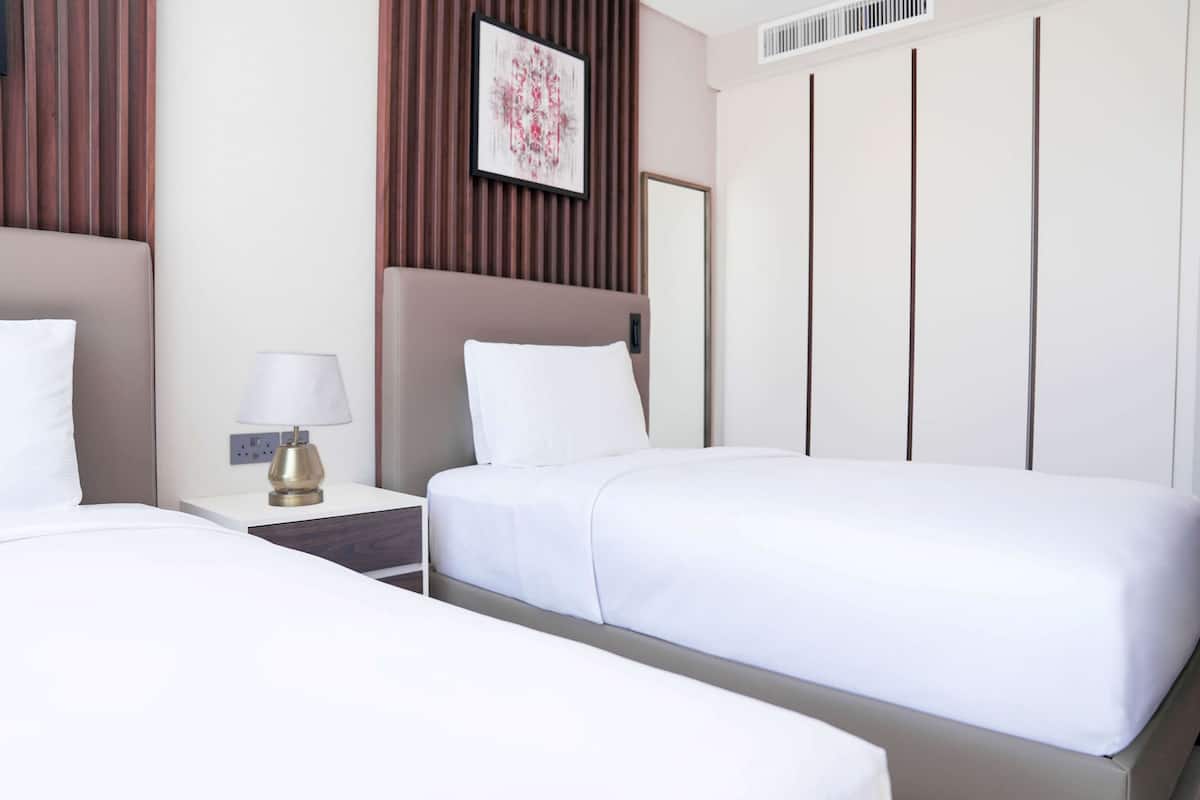 A hotel room with two beds, a bedside table with a lamp, a framed picture on the wall, and a wardrobe.