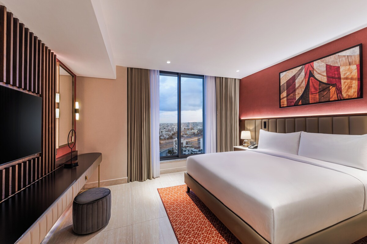 Une chambre d’hôtel moderne dotée d’un grand lit, d’une télévision, d’un bureau et offrant une vue sur la ville.