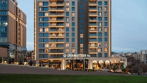 A modern hotel with multiple floors, a well-lit entrance, and a landscaped area in front. - Doubletree By Hilton Amman Hotel & Residences (Amman)