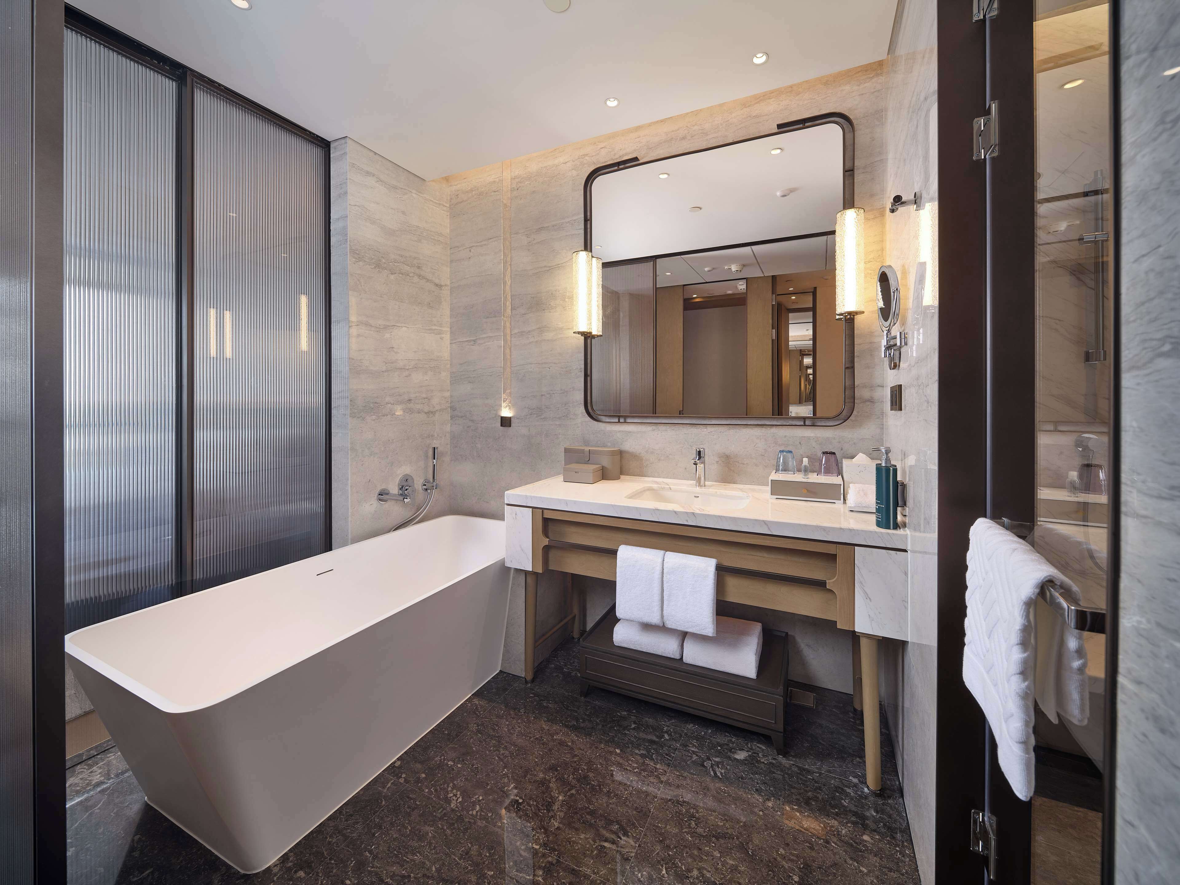 Een moderne badkamer met een vrijstaand bad, een grote spiegel en een wastafelmeubel met een wastafel en handdoekhouder.