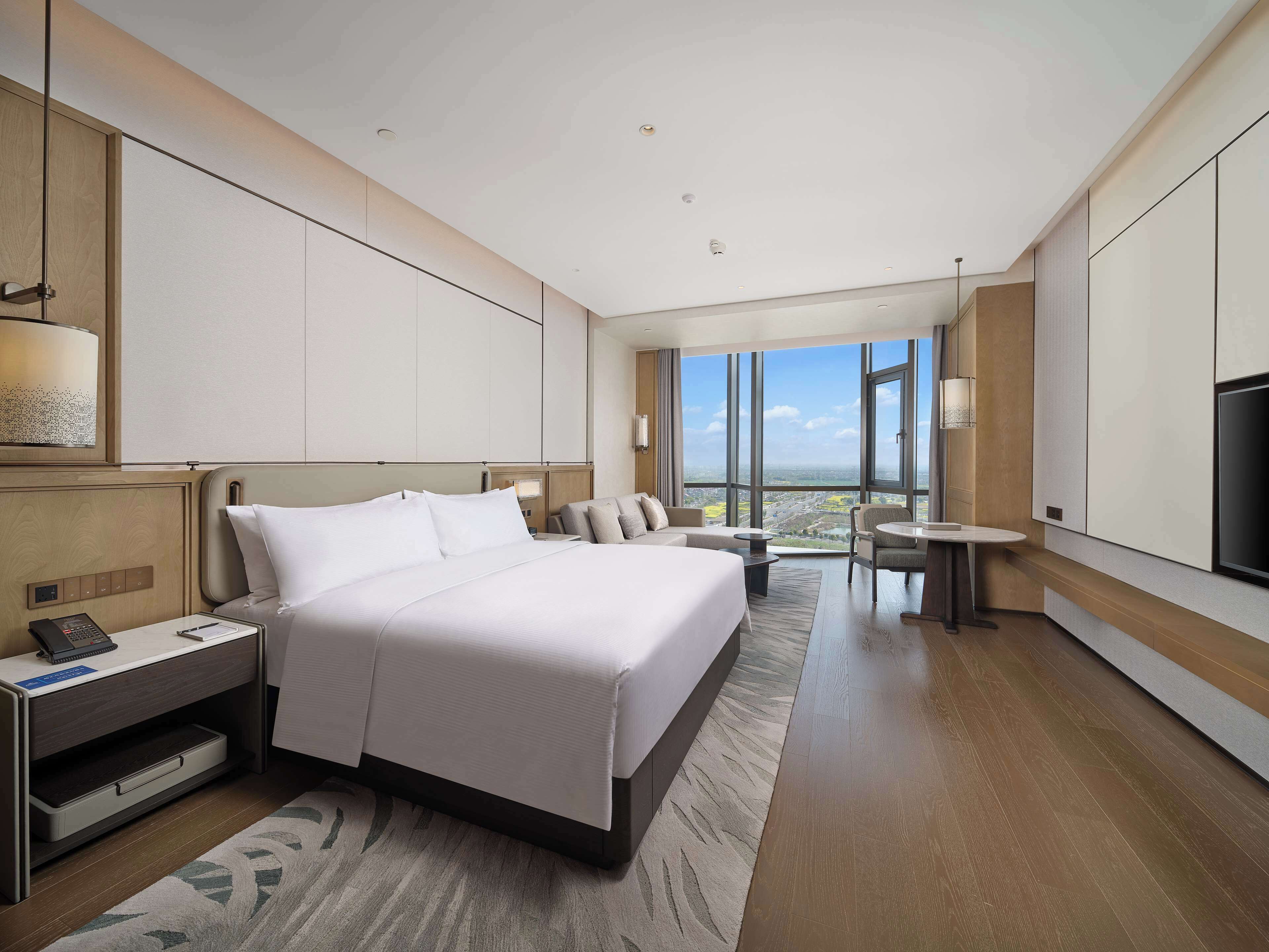 A modern hotel room with a large bed, a desk, a chair, and a TV.