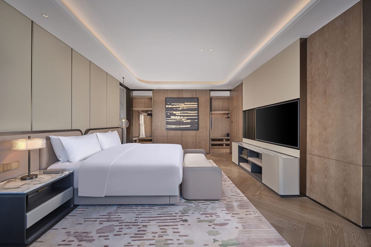 Un dormitorio moderno de hotel con una cama grande, televisión y vestidor.