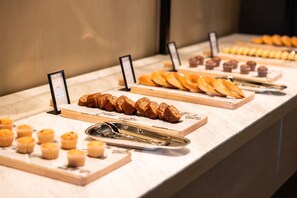 A buffet with various baked goods including bread, pastries, and muffins. - Hilton Jiashan (Jiaxing)