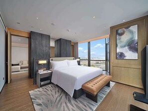 A modern hotel room with a large bed, a bench, a desk, and a view of the city. - Hilton Jiashan (Jiaxing)