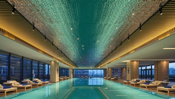 Una piscina interior amplia con zonas de descanso a ambos lados, grandes ventanales y un diseño de techo moderno.