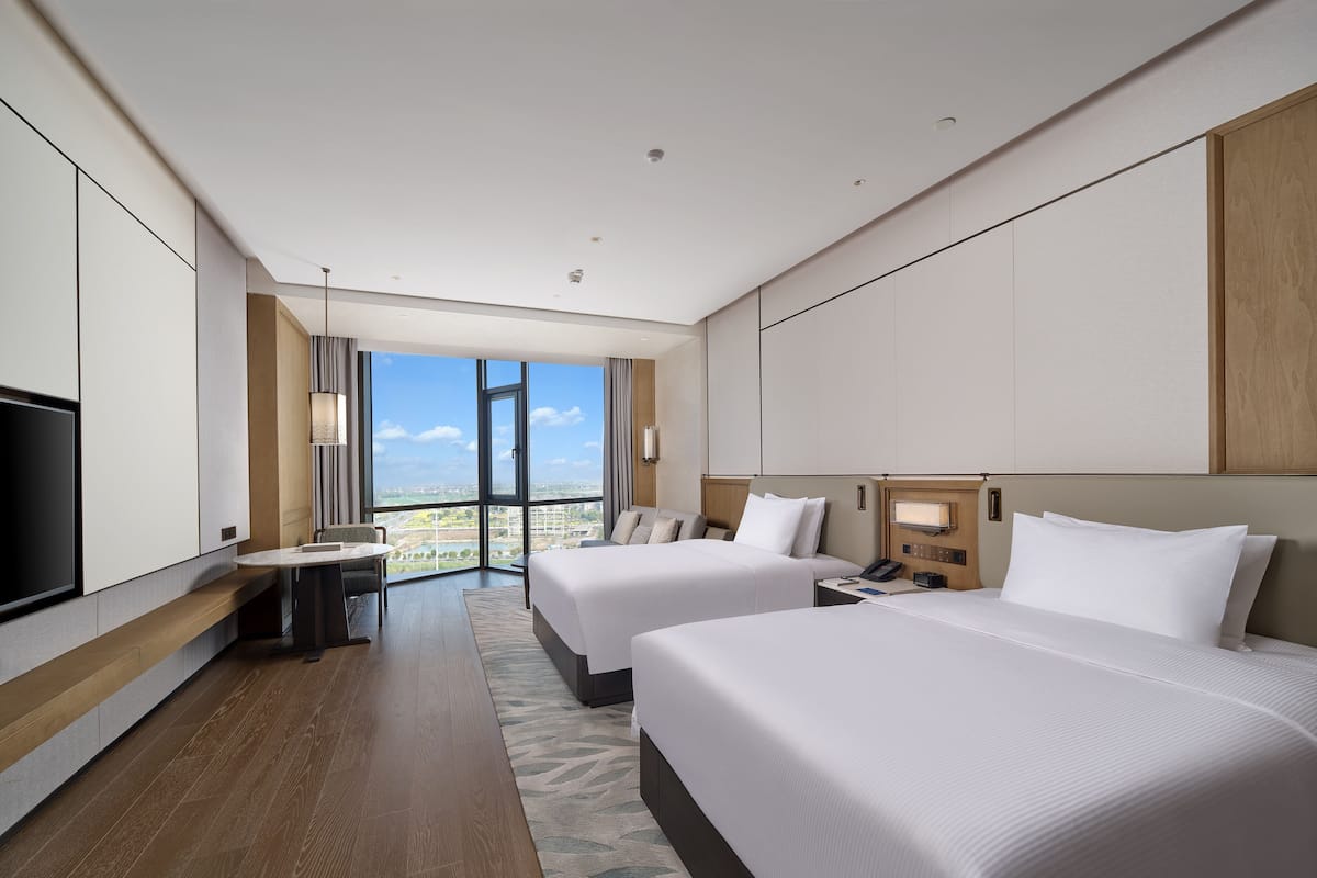 Una habitación de hotel moderna con dos camas, un escritorio, un televisor y un amplio ventanal con vista a la ciudad.