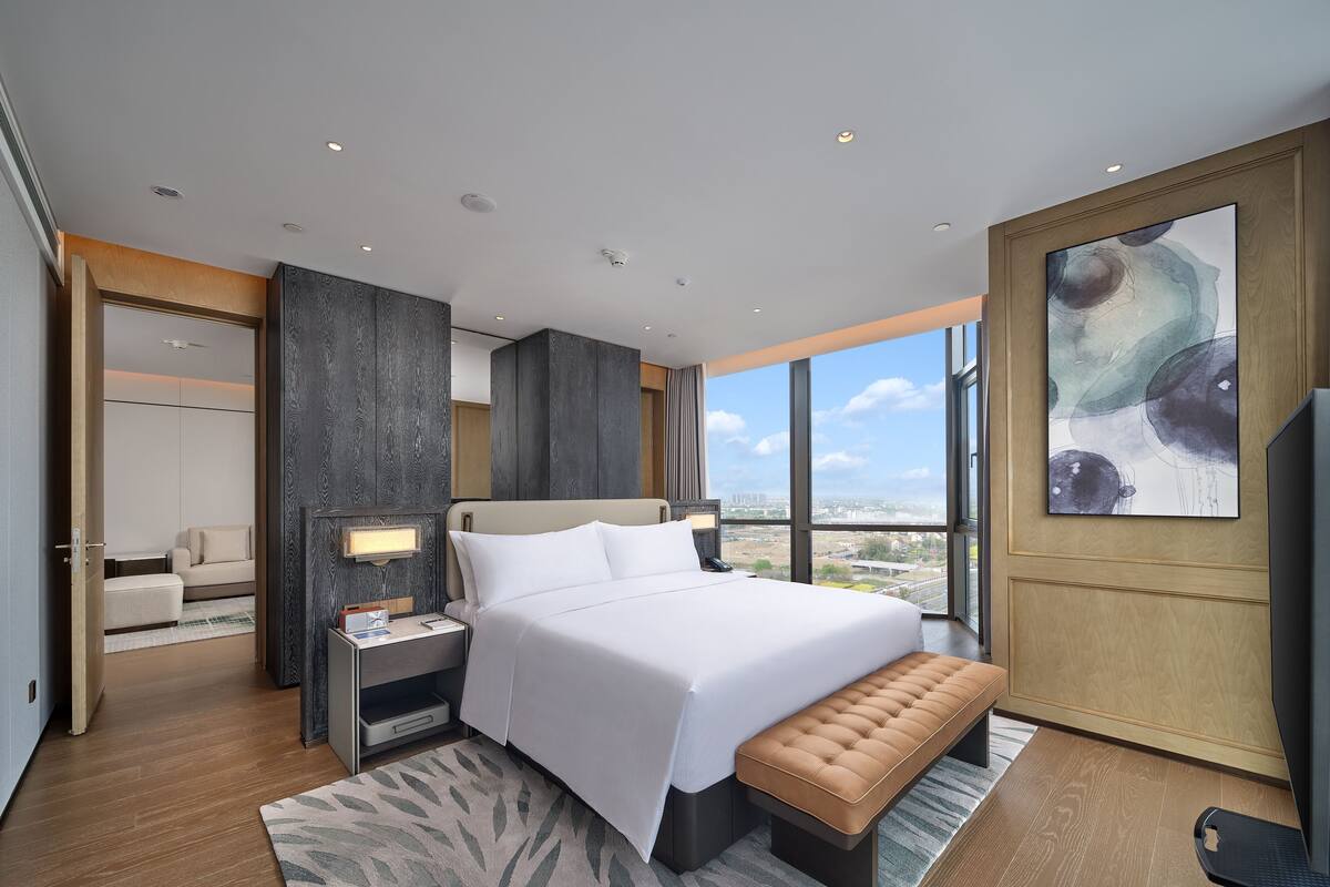 Una habitación de hotel moderna con una cama grande, un banco, un escritorio y vistas a la ciudad.