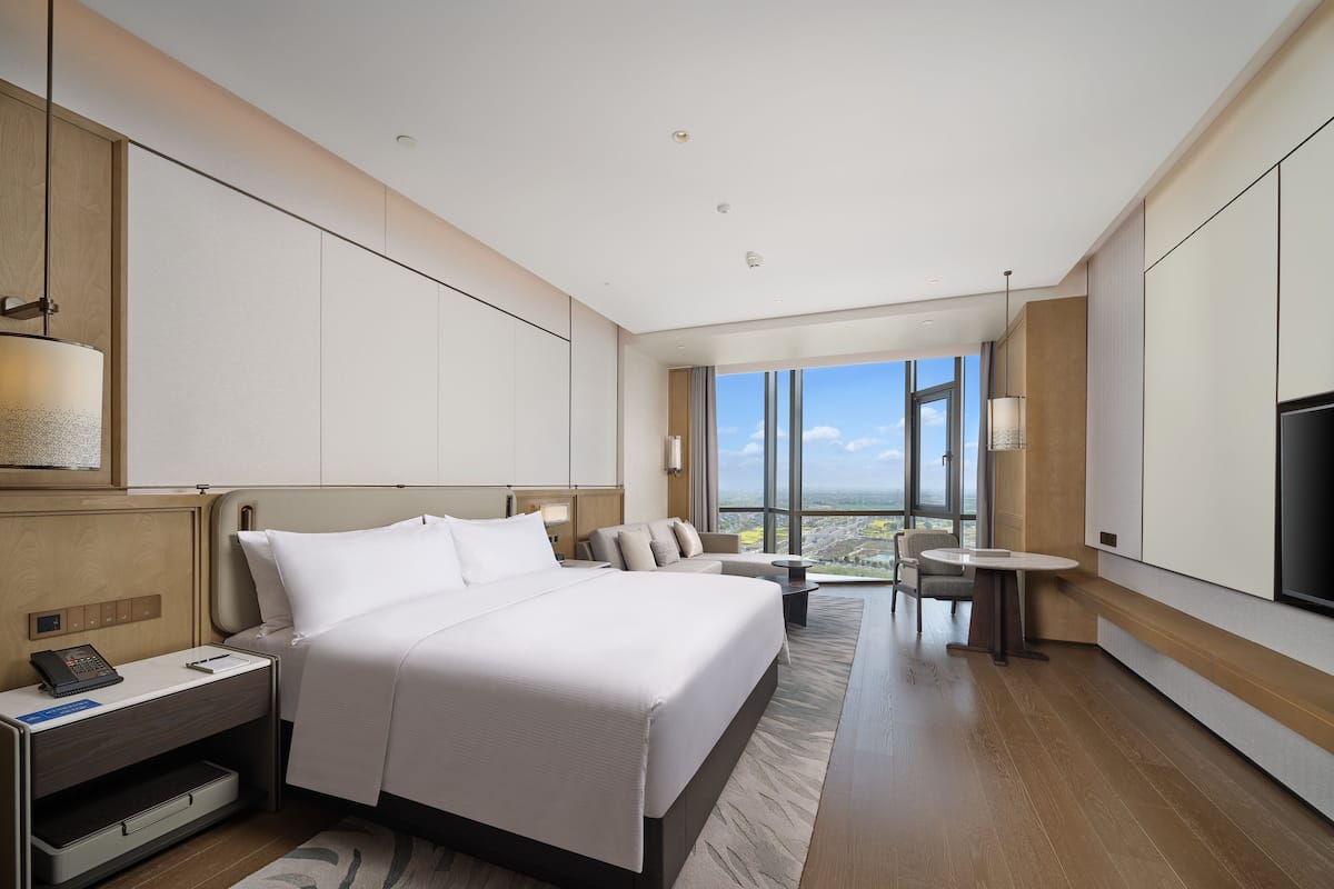 Una habitación de hotel moderna con una cama grande, un escritorio, una silla y un televisor. La habitación tiene un ventanal con vistas a la ciudad.