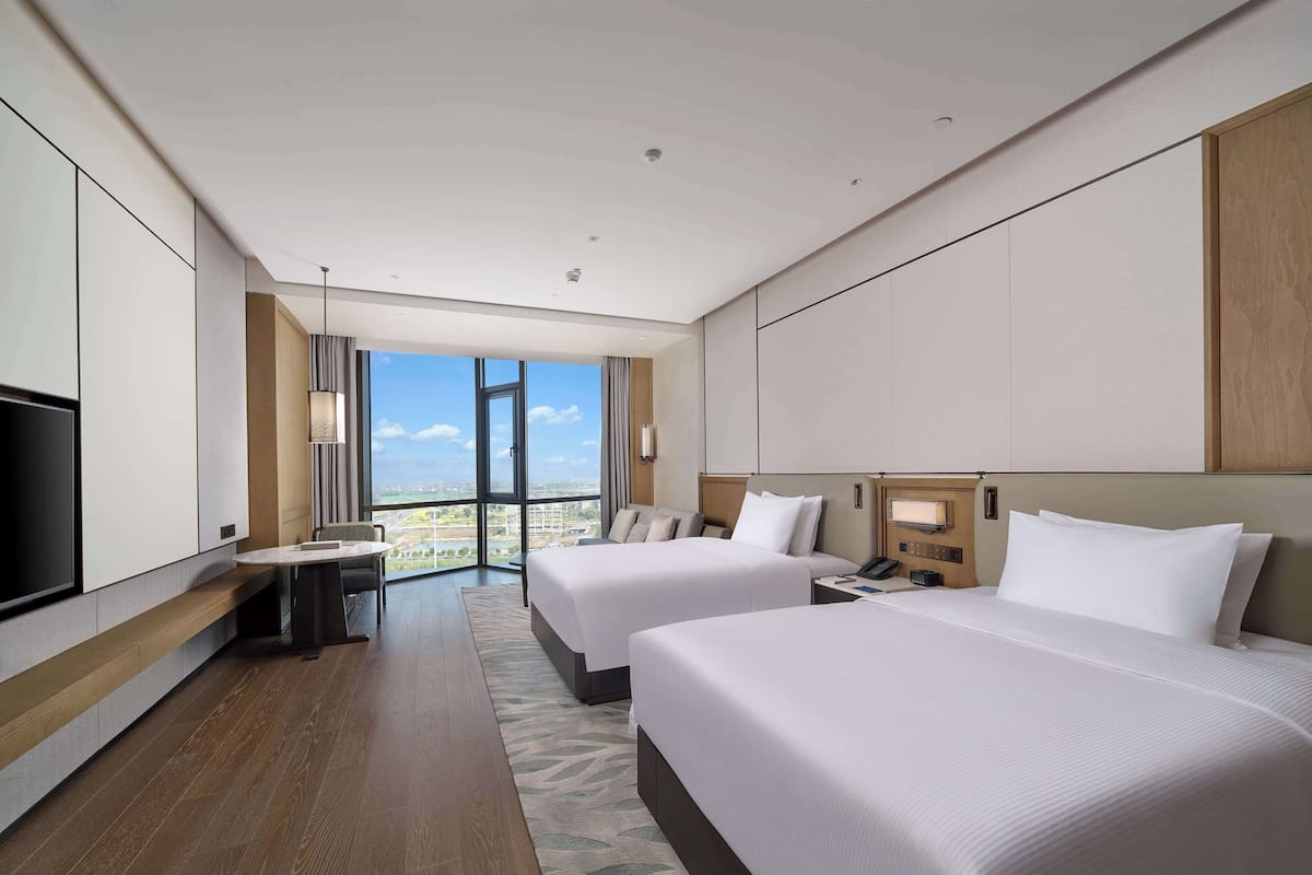 Habitación de hotel moderna con dos camas, un escritorio y un amplio ventanal con vista a la ciudad.